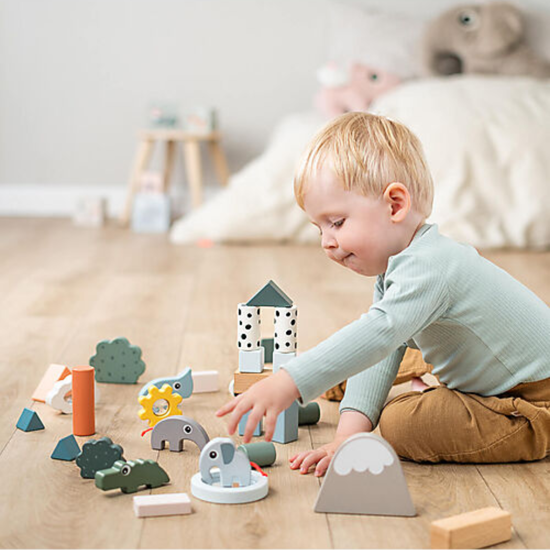 Bambino che gioca con il Set Costruzioni di Legno Deer Friends, torri costruite e animali in legno su pavimento.