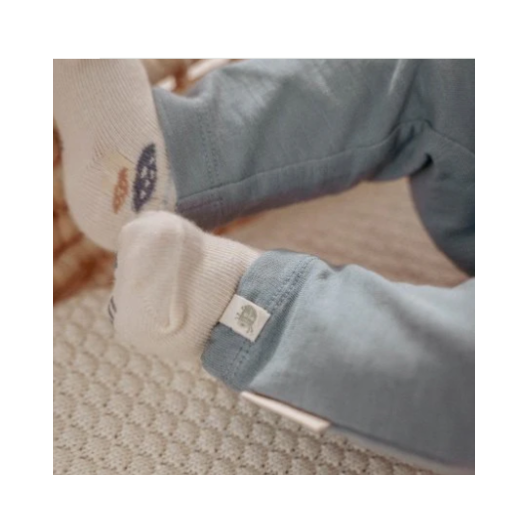 Dettaglio del fondo gamba dei pantaloni blu Little Dutch indossati da un neonato, con etichetta del brand visibile e calzini con stampa bosco.