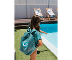 Bambino al mare con zaino anti sabbia Monnëka Whale Teal sulle spalle
