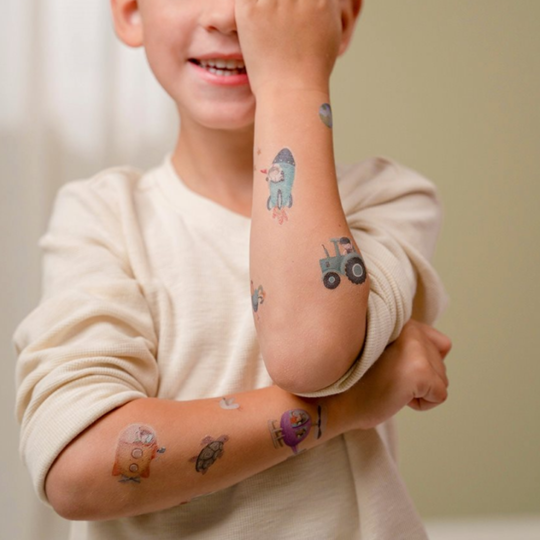 Bambino felice che mostra i tatuaggi Little Dutch con disegni di animali e mezzi di trasporto.