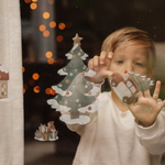 Bambina applica un adesivo natalizio di Babbo Natale su una finestra, creando una decorazione festiva con il Kit Adesivi Little Dutch.