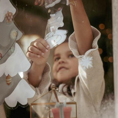 Bambino applica gli adesivi Little Dutch per finestra, creando una decorazione con albero di Natale e ornamenti festivi.