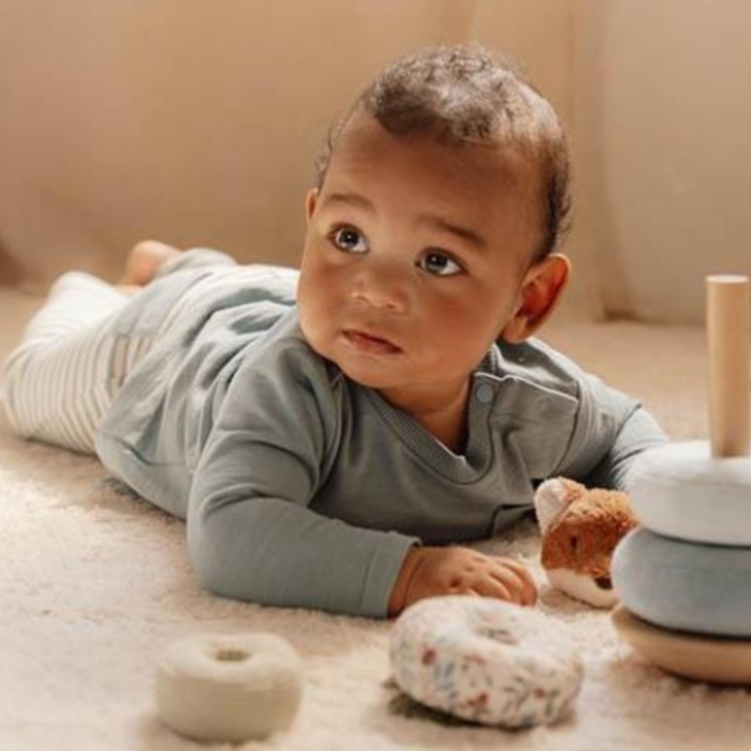 Bambino che esplora gli anelli di stoffa del gioco impilabile Little Dutch, disteso su un tappeto.