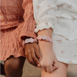 Due bambine che indossano braccialetti creati con il set perline per braccialetti di Little Dutch, con dettagli floreali e colori pastello.