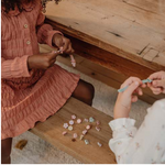 Due bambine sedute che mostrano i loro braccialetti personalizzati, realizzati con il kit braccialetti bambina Fairy Garden di Little Dutch.