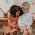 Due bambine che indossano braccialetti creati con il set perline per braccialetti di Little Dutch, con dettagli floreali e colori pastello.