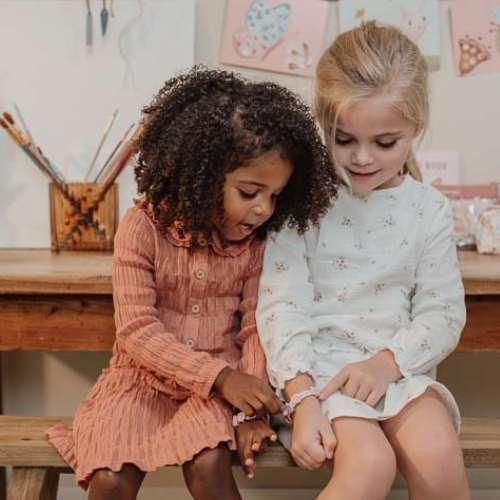 Due bambine che indossano braccialetti creati con il set perline per braccialetti di Little Dutch, con dettagli floreali e colori pastello.