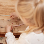 Bambina che gioca con il kit per fare braccialetti di Little Dutch, distribuendo perline gioco su un tavolo di legno.